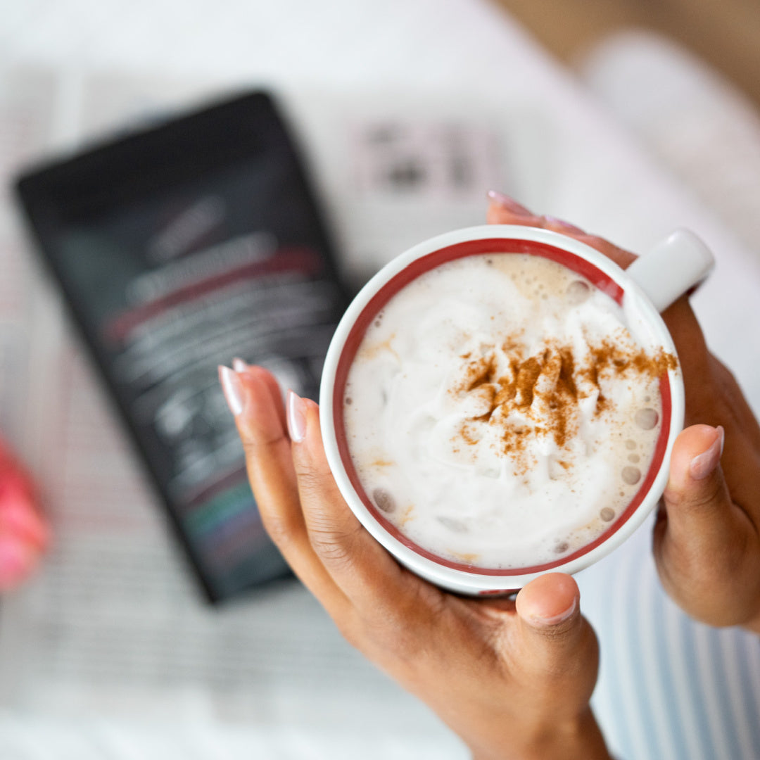 Person holding a cup of mushroom hot chocolate with cinnamon sprinkles, blurred background