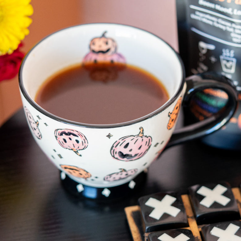 Cup of cacao pumpkin spice, a zplantmagic mushroom koffee drink, with Halloween-themed design, Tic-Tac-Toe game, and pumpkin spice coffee package on a table.