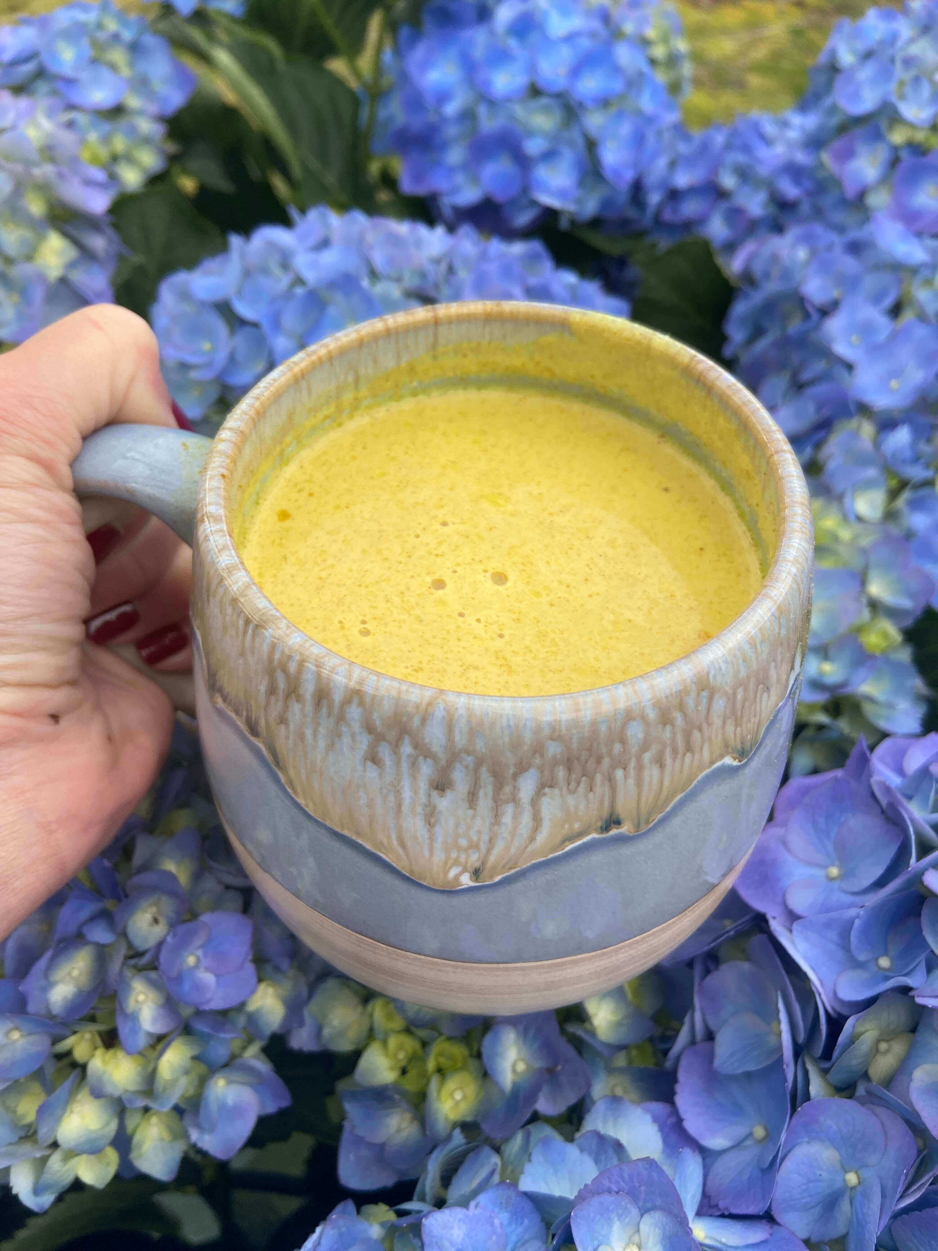 golden milk latte with ghee, honey, and lion's mane mushroom surrounded by violet hydrangeas 