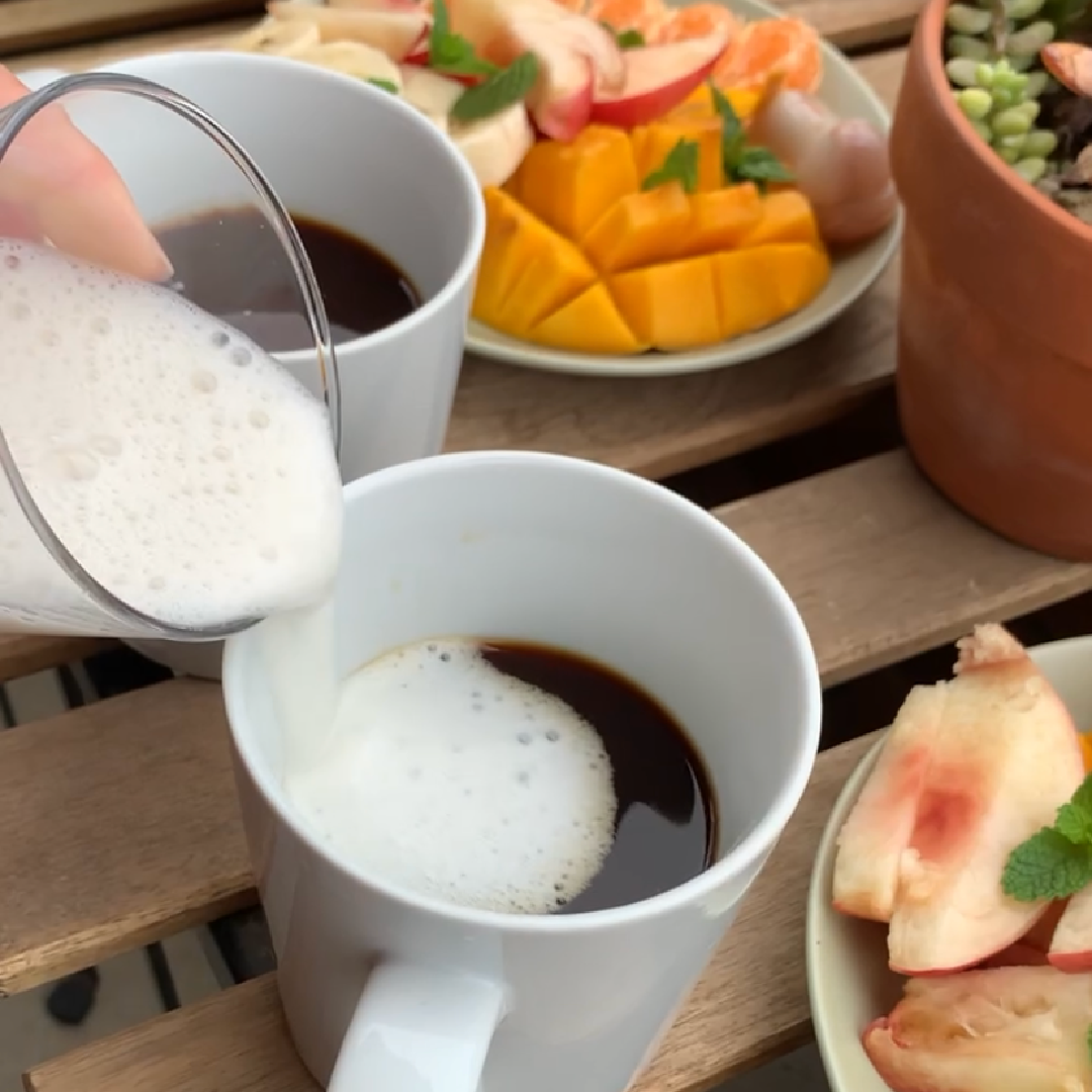 Pouring milk into caffeine-free mushroom coffee during a relaxed morning breakfast ritual with fresh fruit