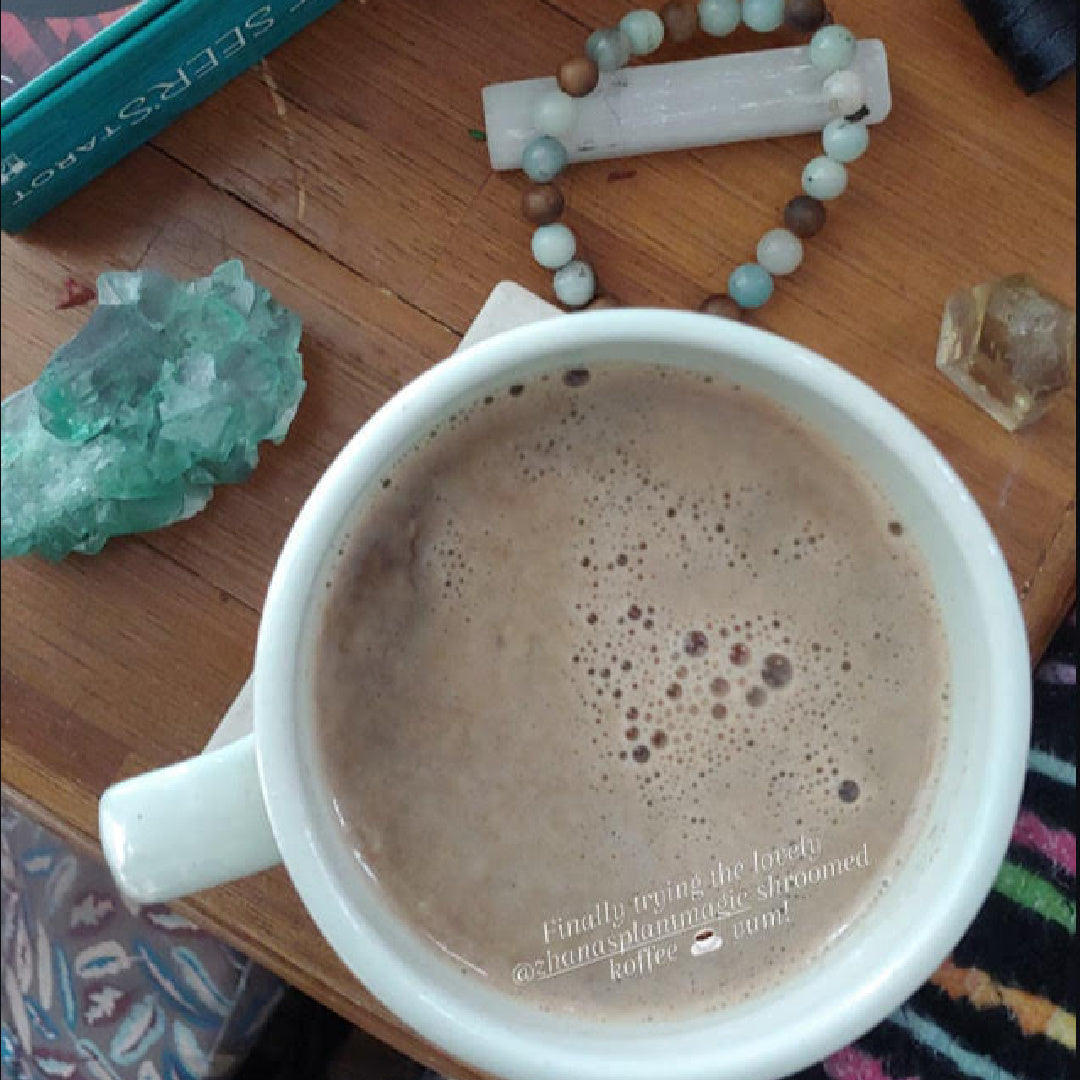 Top view of creamy mushroom koffee latte in a mug during a cozy morning ritual at home with meditation crystals and mala beads
